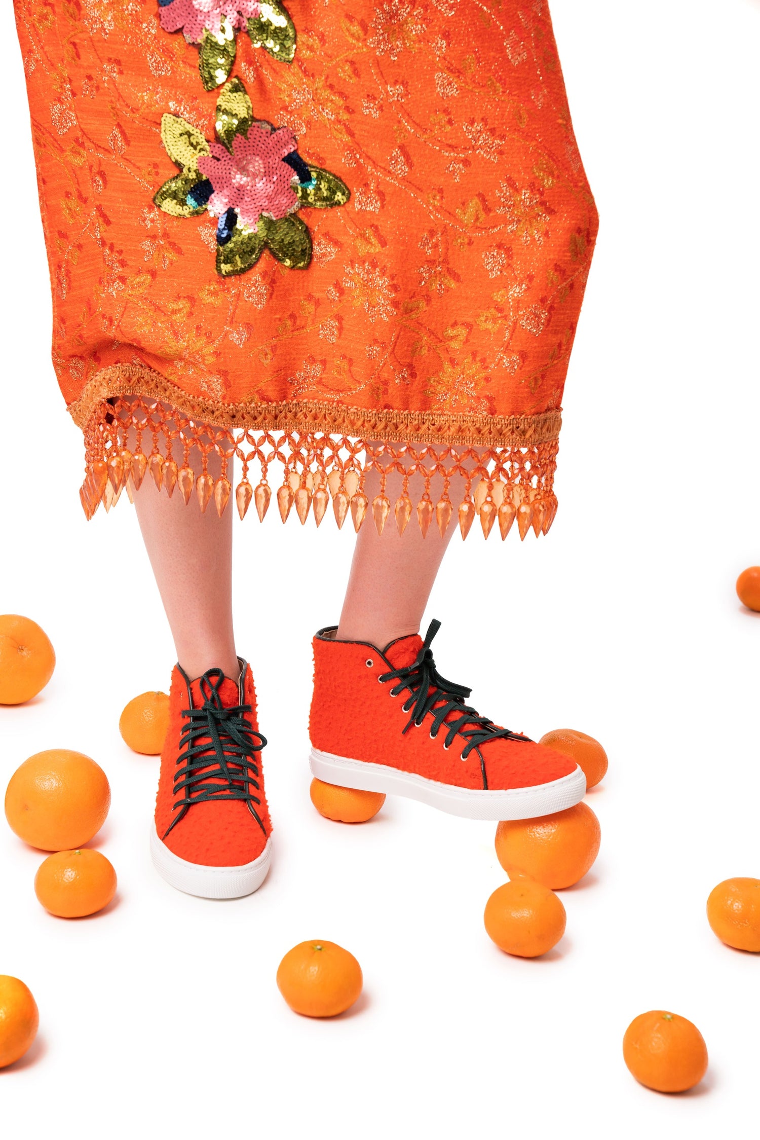 Person wearing orange high-top sneakers with a matching dress amidst oranges on a white background