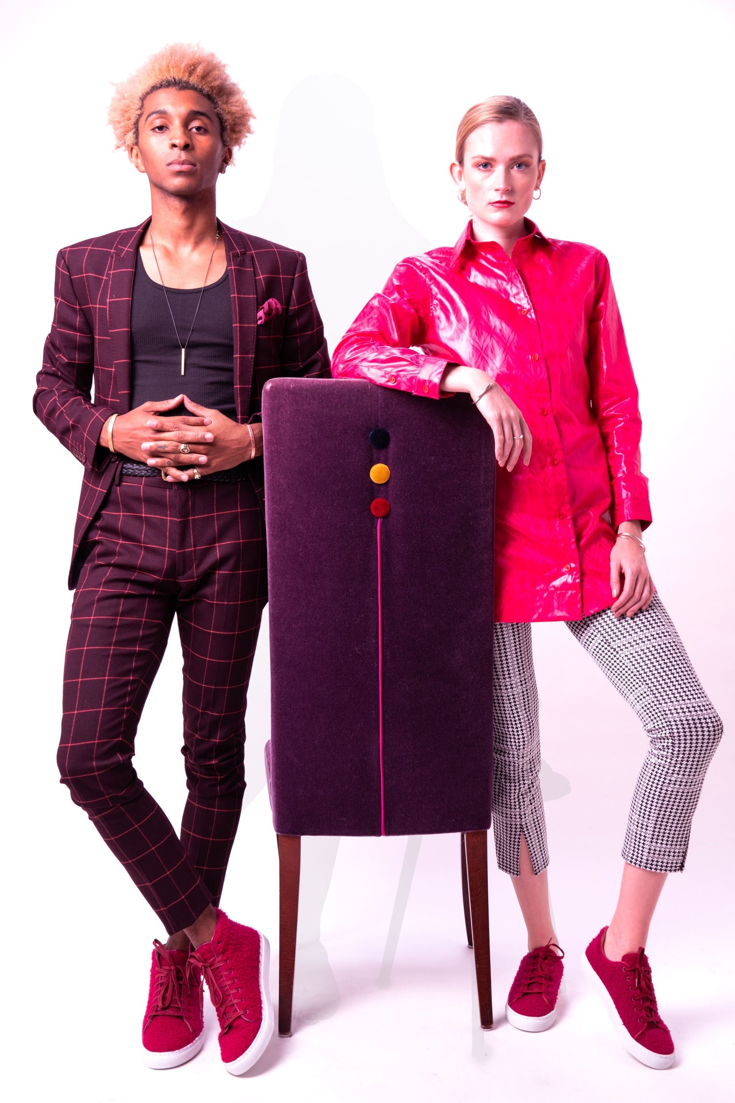 Two people standing next to a purple chair with a large button on a white background