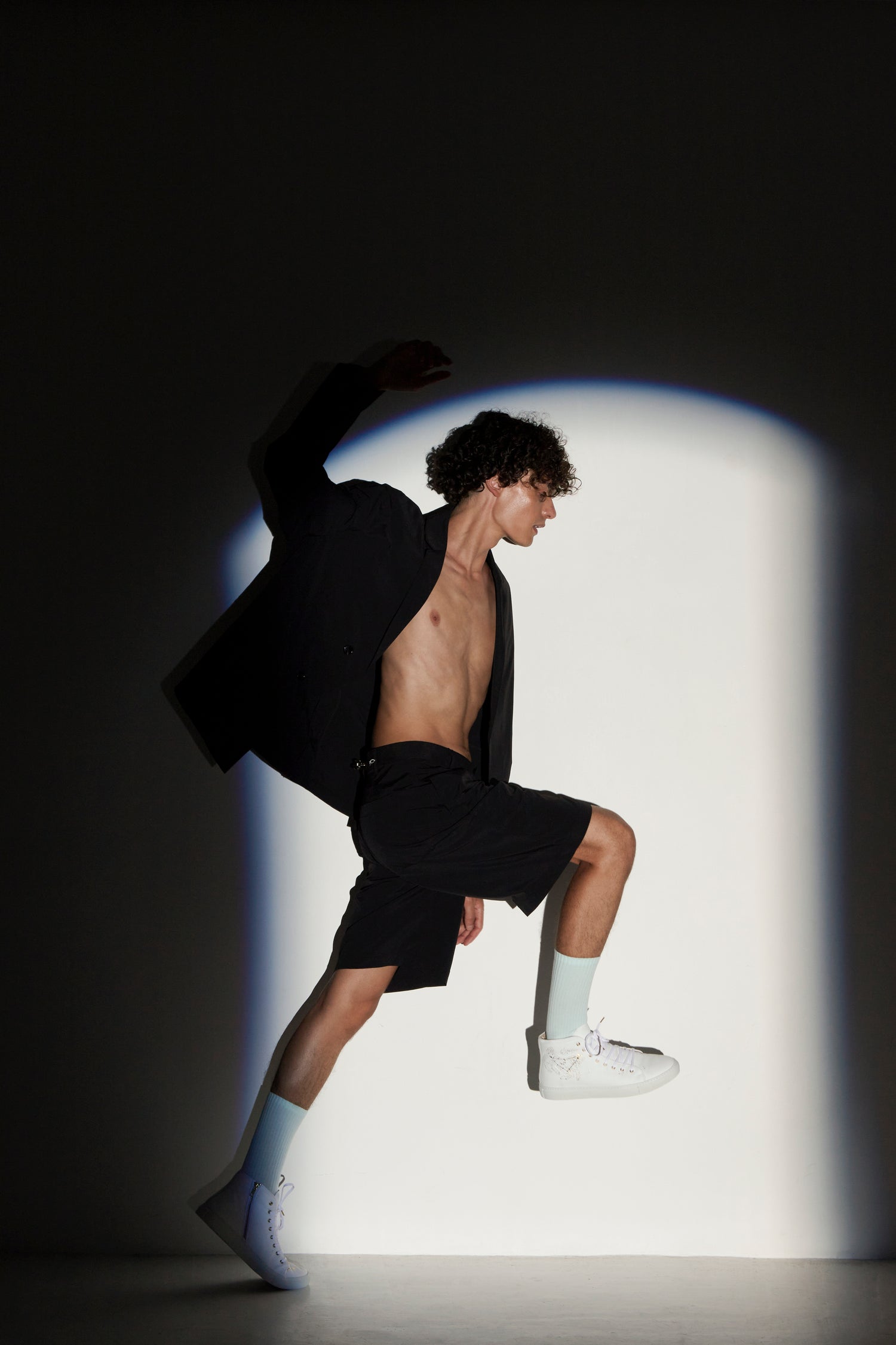 Person in black shorts and white sneakers posing against a light and dark gradient background